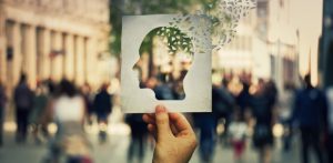 Hand hält Papierbild mit ausgeschnittener Kopfsilhouette vor Menschenmenge auf Platz