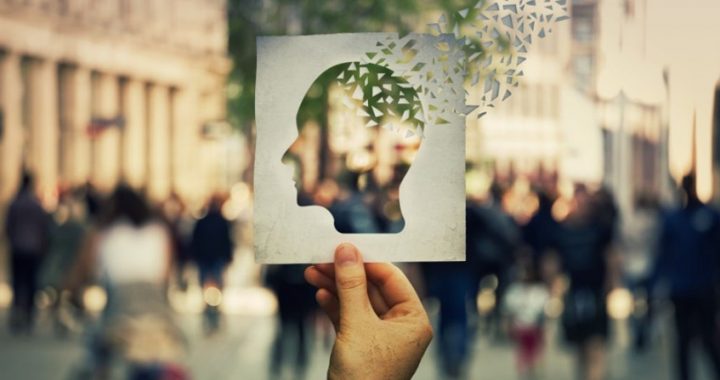 Hand hält Papierbild mit ausgeschnittener Kopfsilhouette vor Menschenmenge auf Platz