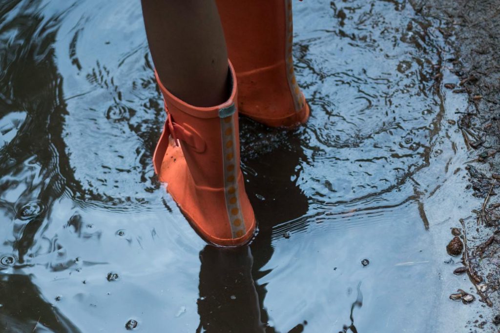 Kind in Gummistiefeln in Pfütze