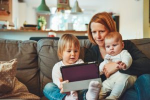 Mutter sitzt mit zwei Kindern auf Couch mit Tablet