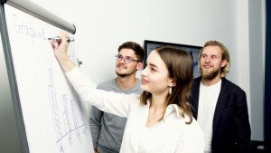 Drei Personen stehen vor Flipchart
