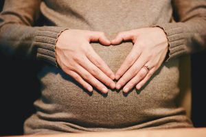 Schwangere bildet mit ihren Händen ein Herz vor ihrem Bauch