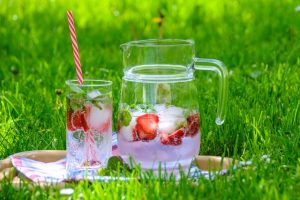 Kanne und Glas mit Wasser und Erdbeeren auf Wiese
